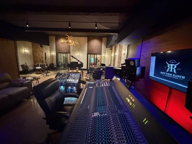 Music production studio with mixing console, speakers, and a large screen displaying Rhythym Ranch logo.