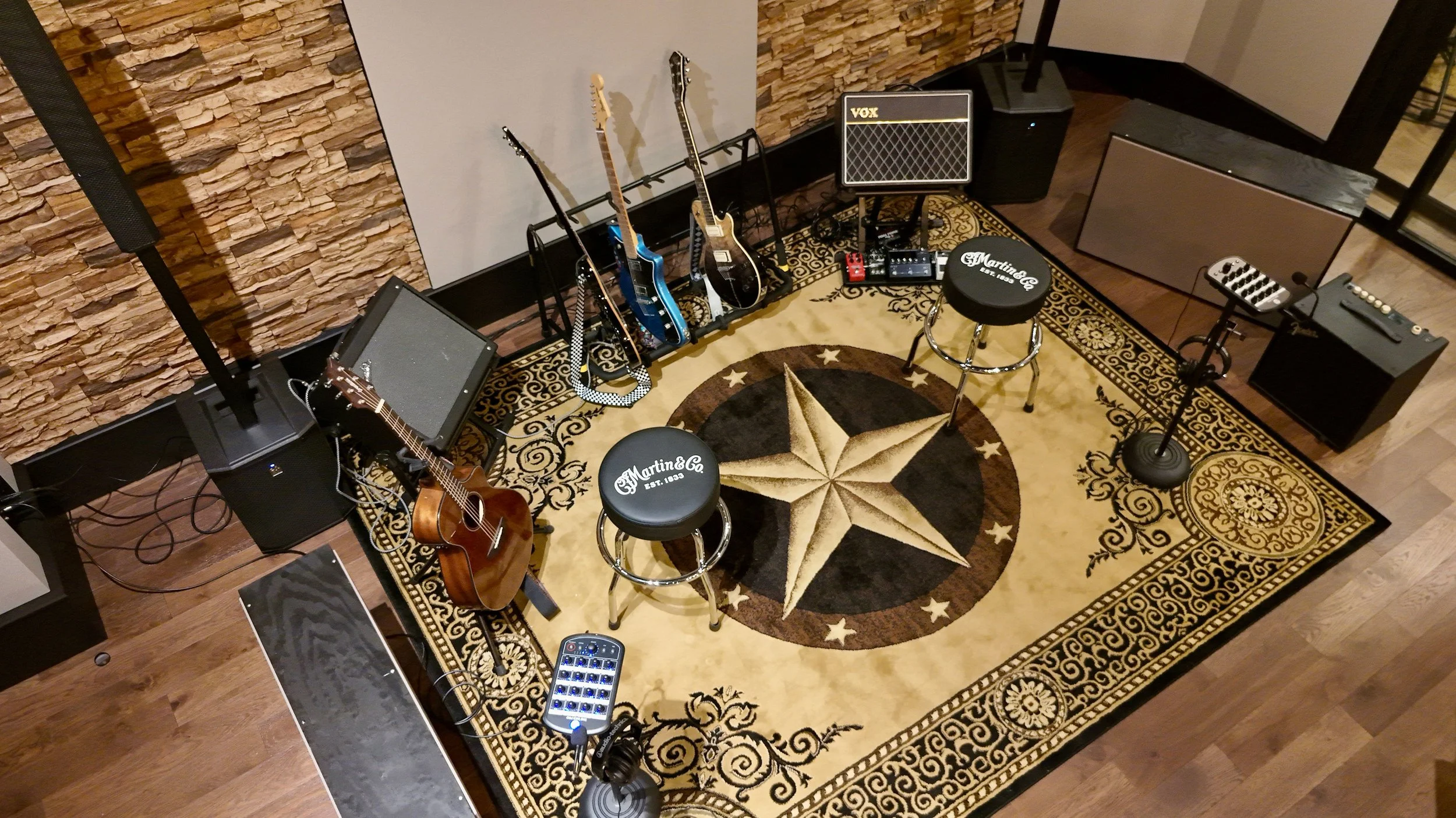 Music studio with guitars, amplifiers, a stool, and a rug with a star design.