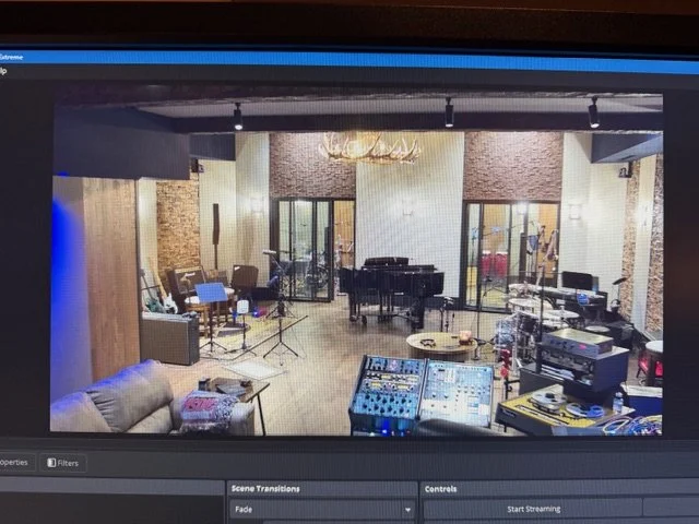 Recording studio with musical instruments, a grand piano, microphones, and sound equipment in a room with exposed brick walls and large windows.
