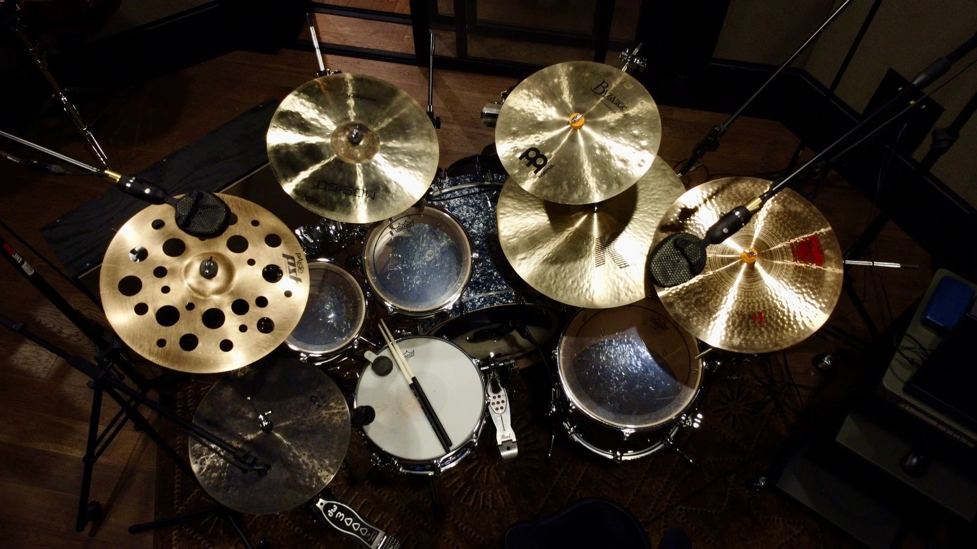 Overhead view of a drum set with various cymbals, drums, drumsticks, microphones, and music stand on a wooden floor.