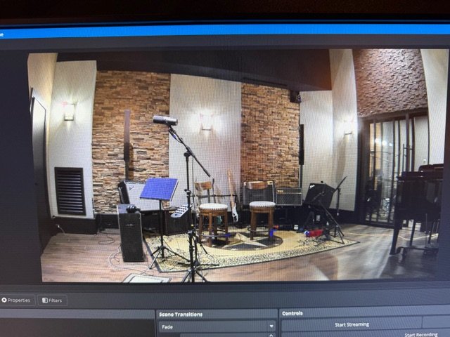 Music recording studio with microphones, chairs, a music stand, and musical equipment, with brick and textured walls.
