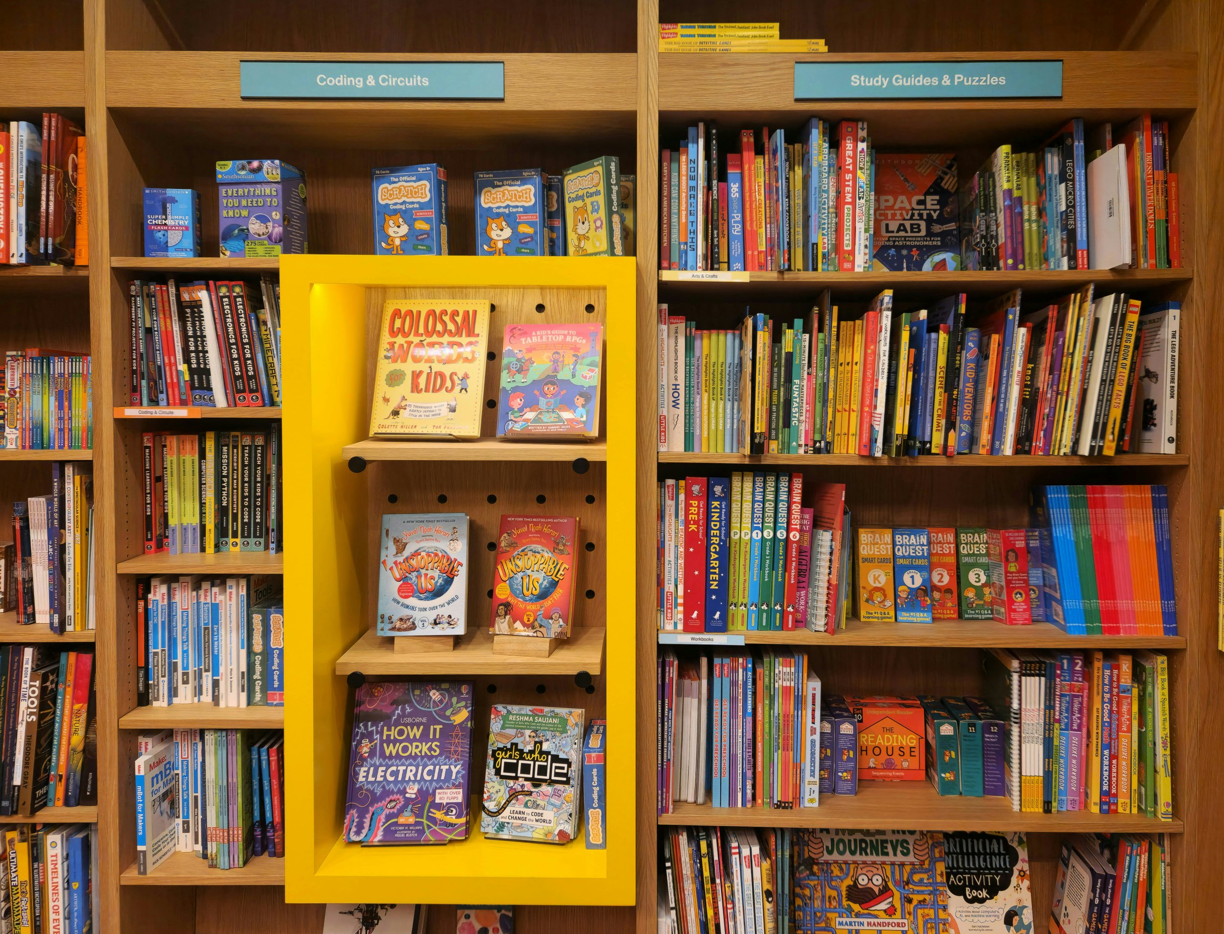 Bookshelves with educational books, divided into sections labeled 'Coding & Circuits' and 'Study Guides & Puzzles.' Items include books on electricity, coding, puzzles, and science.