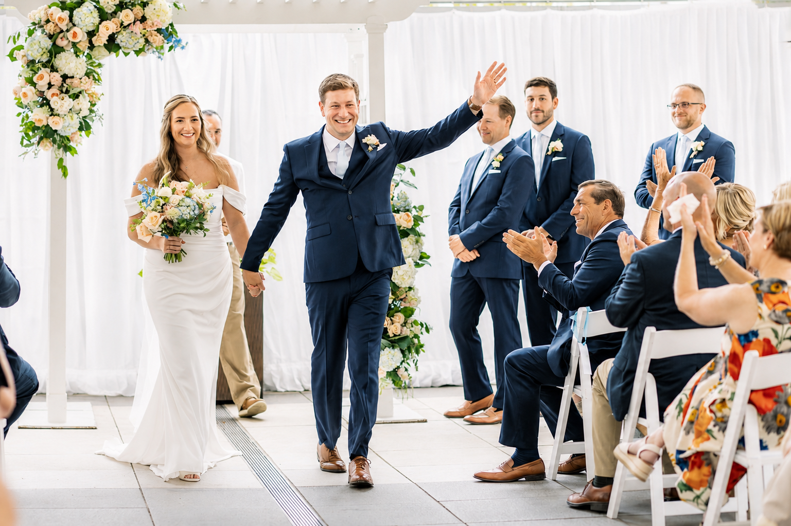 Newlyweds celebrating as they walk back down the aisle while guests applaud at an outdoor tent ceremony