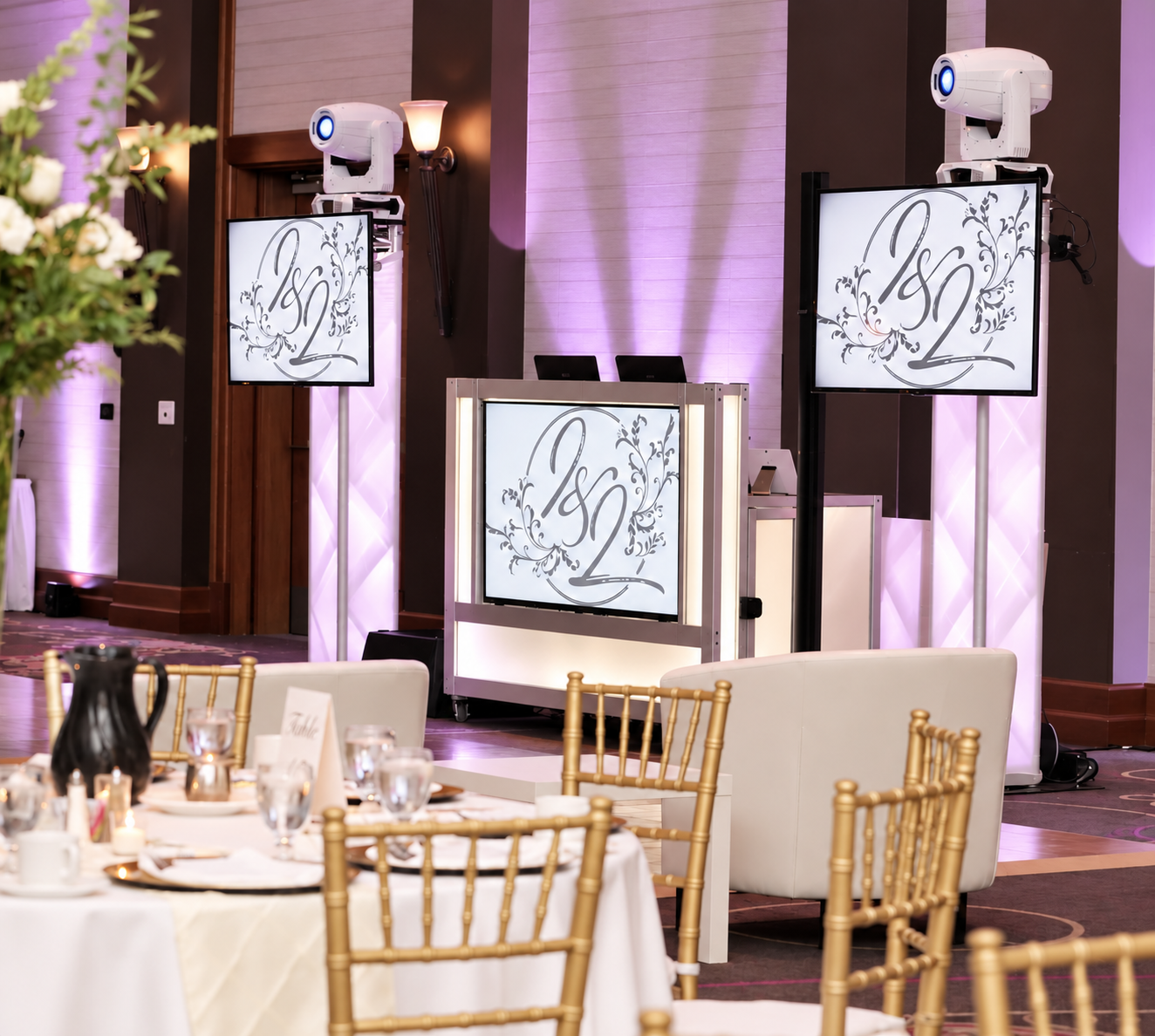 NightBeat DJ booth with TV screens showing the couple's monogram, moving-head lights and purple uplighting