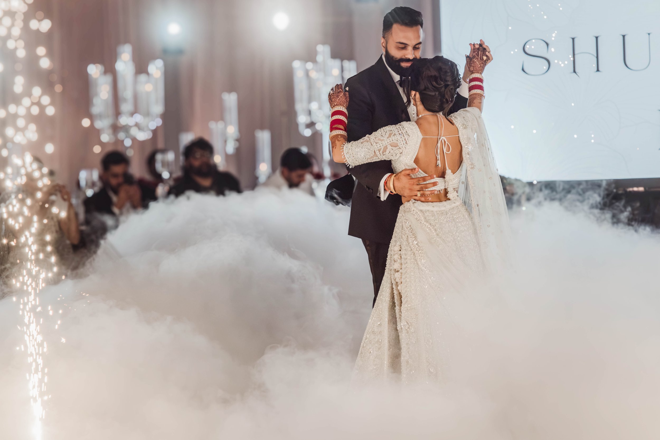 Couple dancing on a low cloud of dry ice with cold spark fountains behind them