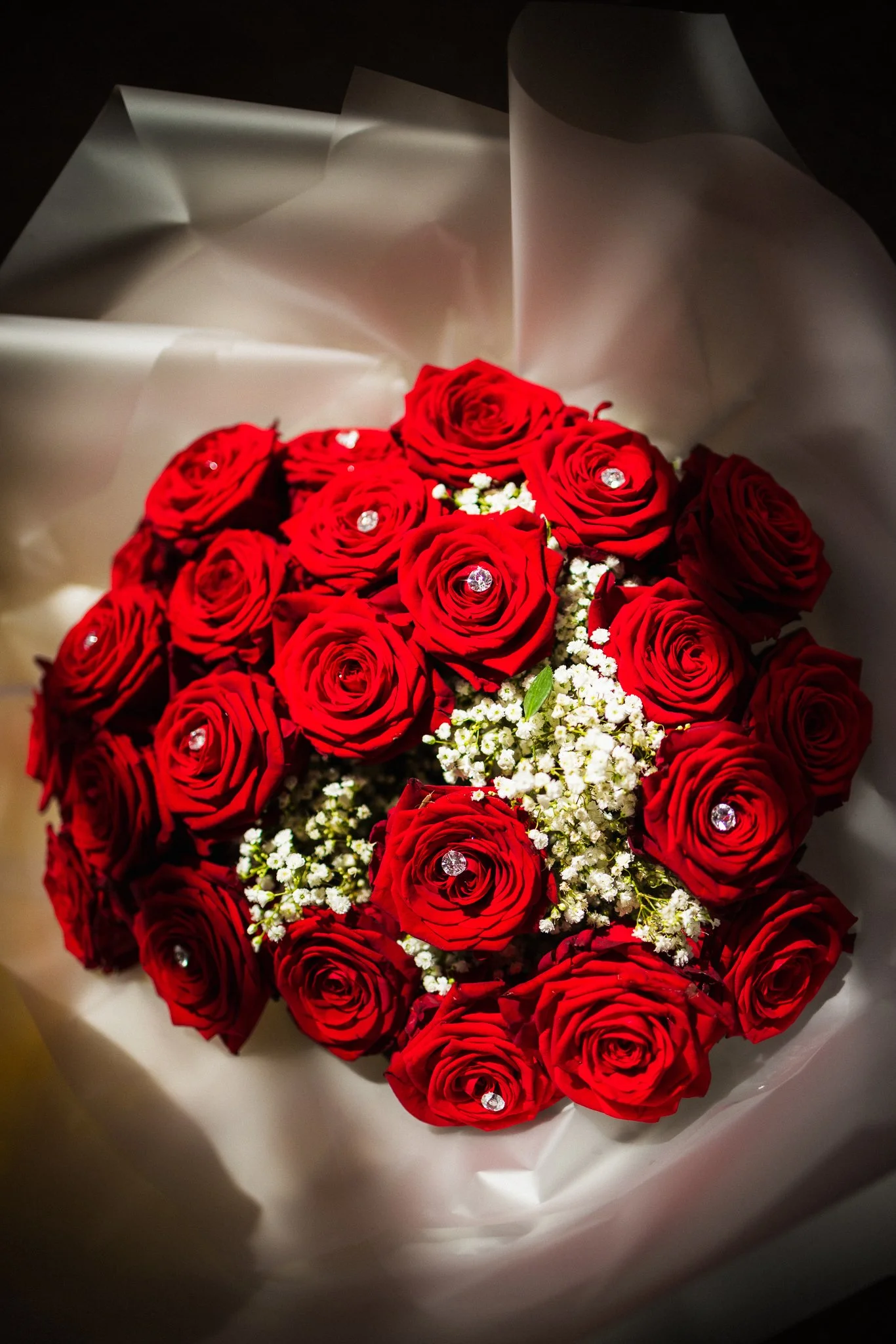 Bouquet of red roses with small white filler flowers wrapped in white paper.