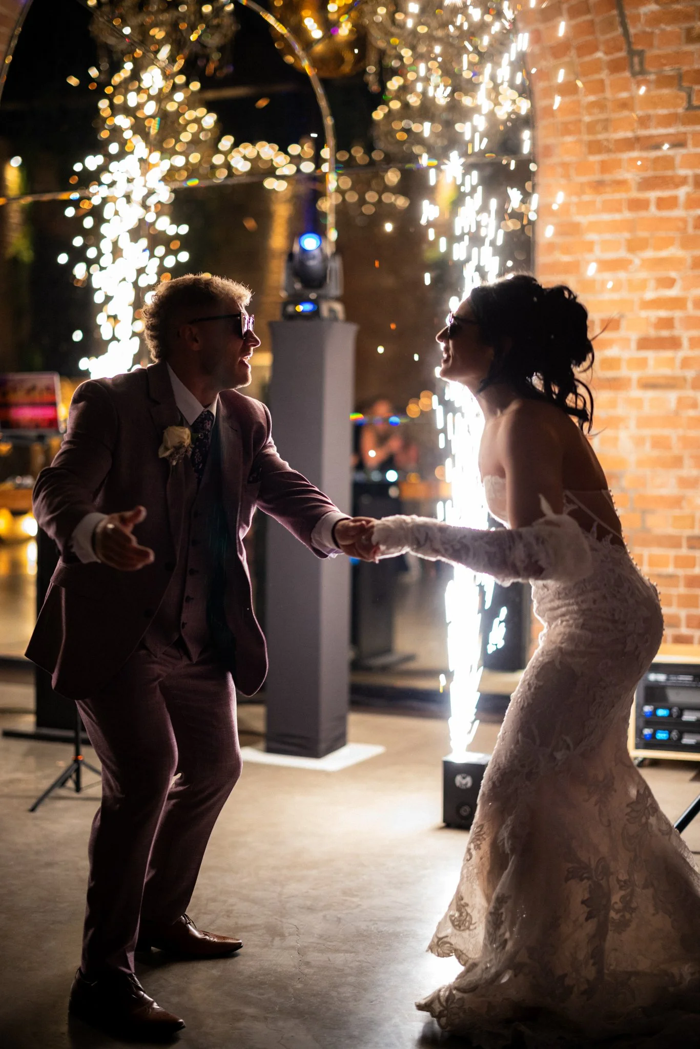 A couple dancing at a wedding reception at night, with fireworks in the background.