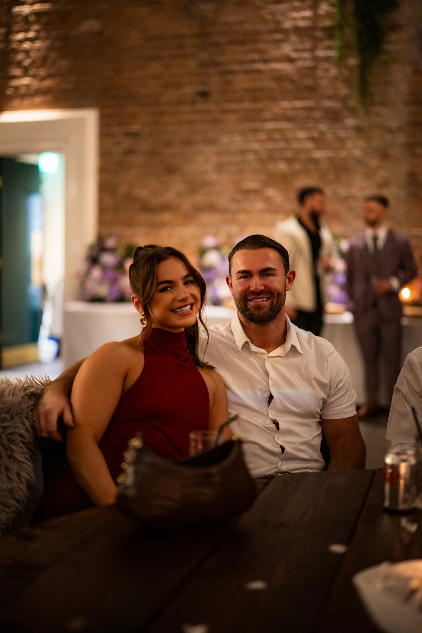 People sitting at a table in a dimly lit restaurant with a brick wall background, smiling for the camera.