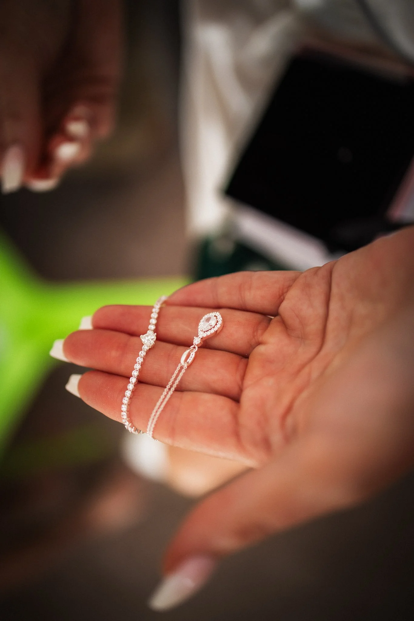 Close-up of a person's hand holding several pieces of jewelry, including a diamond bracelet, a diamond ring, and a silver necklace, with a blurred background.