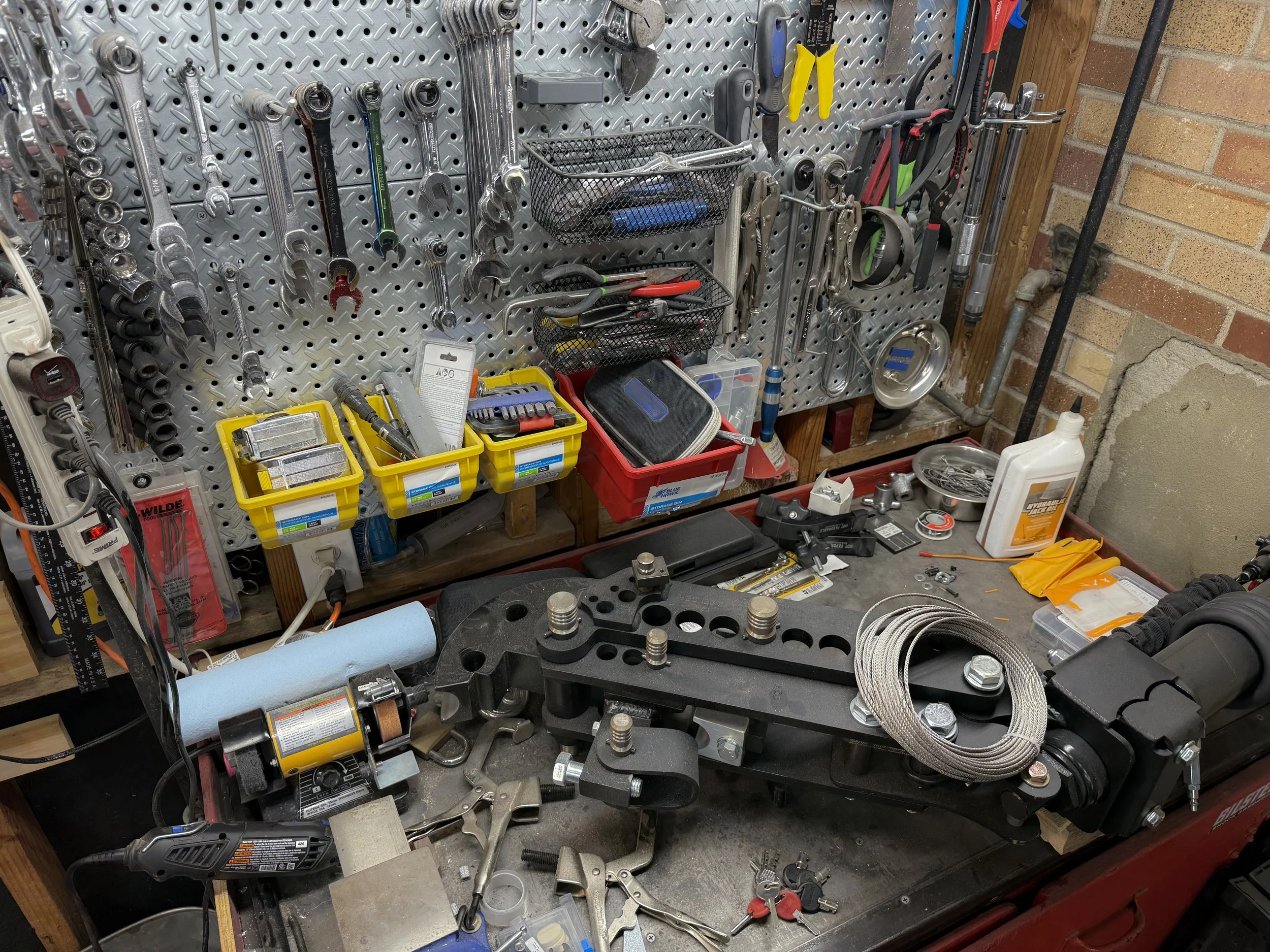 A pegboard filled with various hand tools such as wrenches, pliers, screwdrivers, and a socket set, with some power tools and small containers on a workbench below.