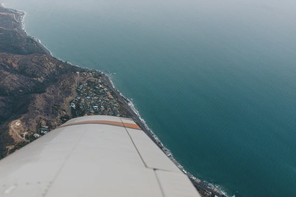 An aerial view from an airplane showing a coastline with houses and roads adjacent to the ocean.