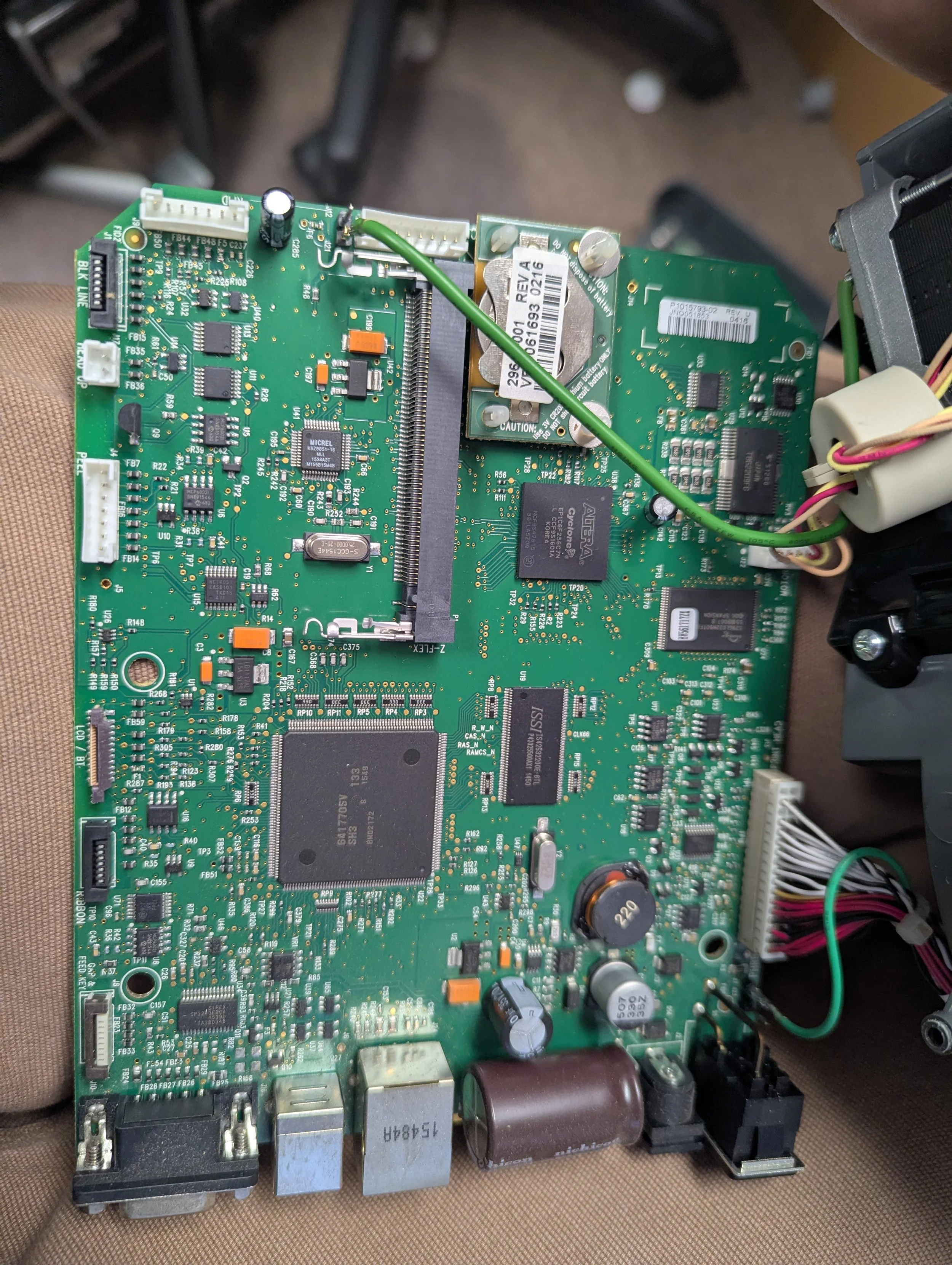 Close-up of a green circuit board filled with electronic components, including capacitors, resistors, chips, and connectors, with wires attached.
