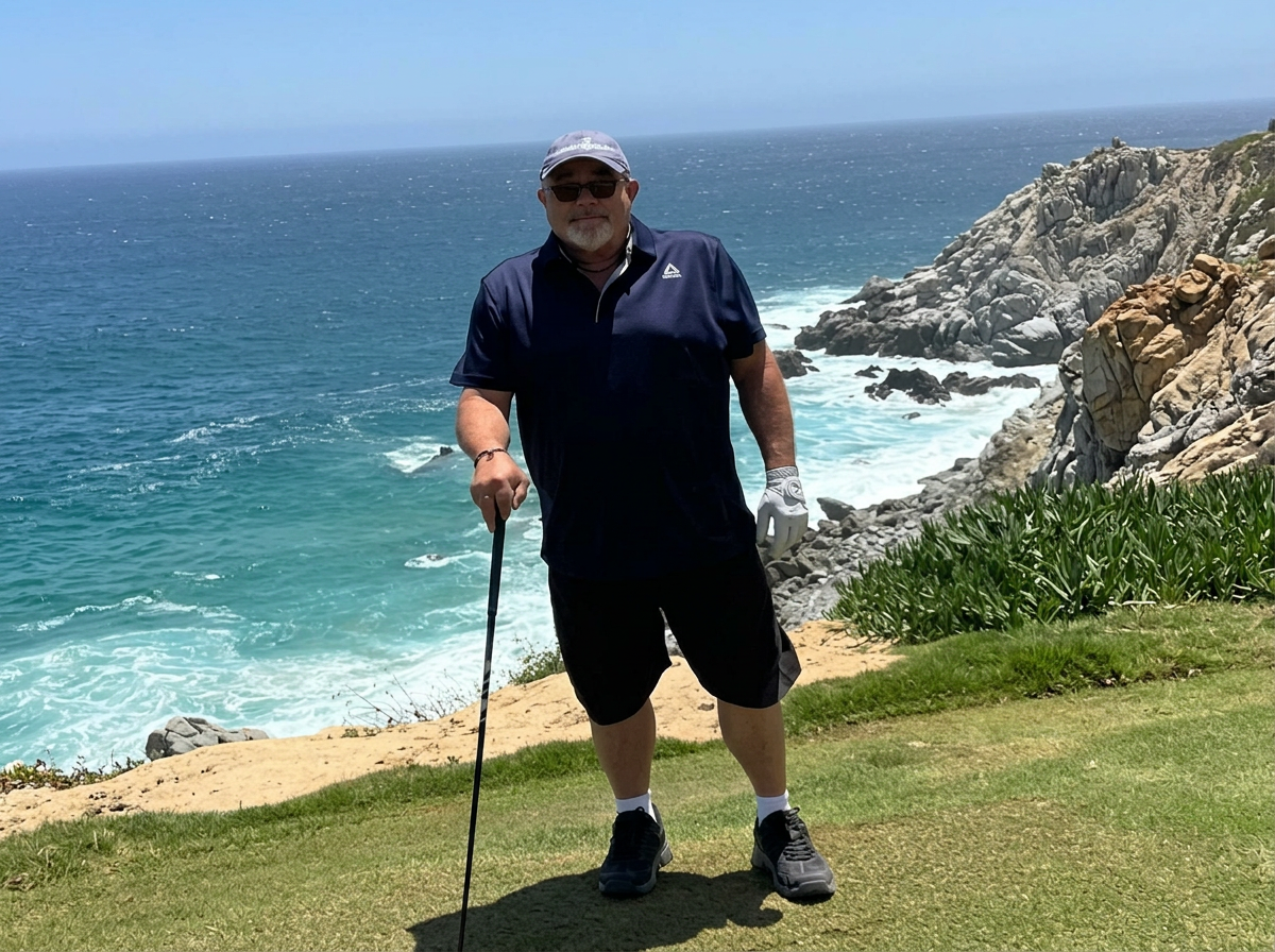 A man stands on a grassy area near the coast, holding a golf club, with rocky cliffs and the ocean in the background on a sunny day.