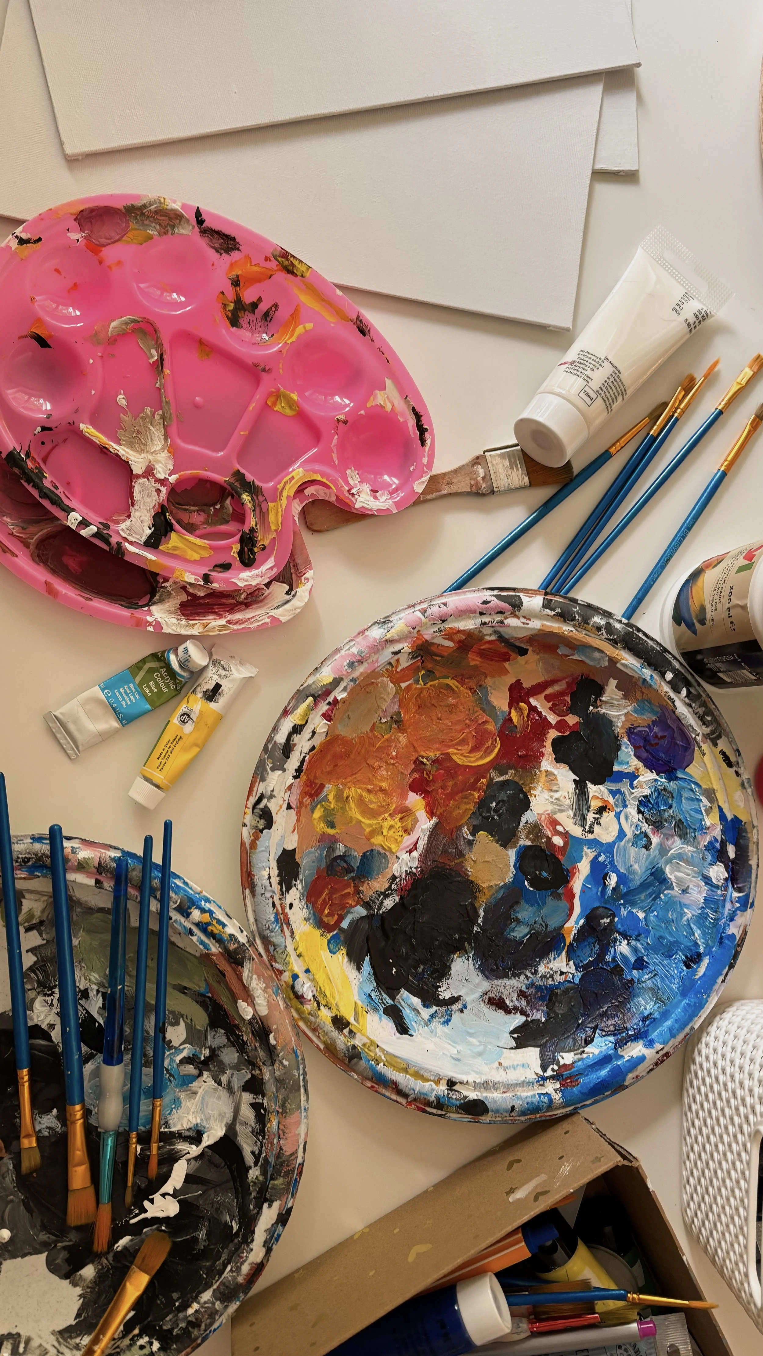 Malkittel, Farbpalette, Pinsel, Tube und Farben für die Malerei auf einem Tisch.