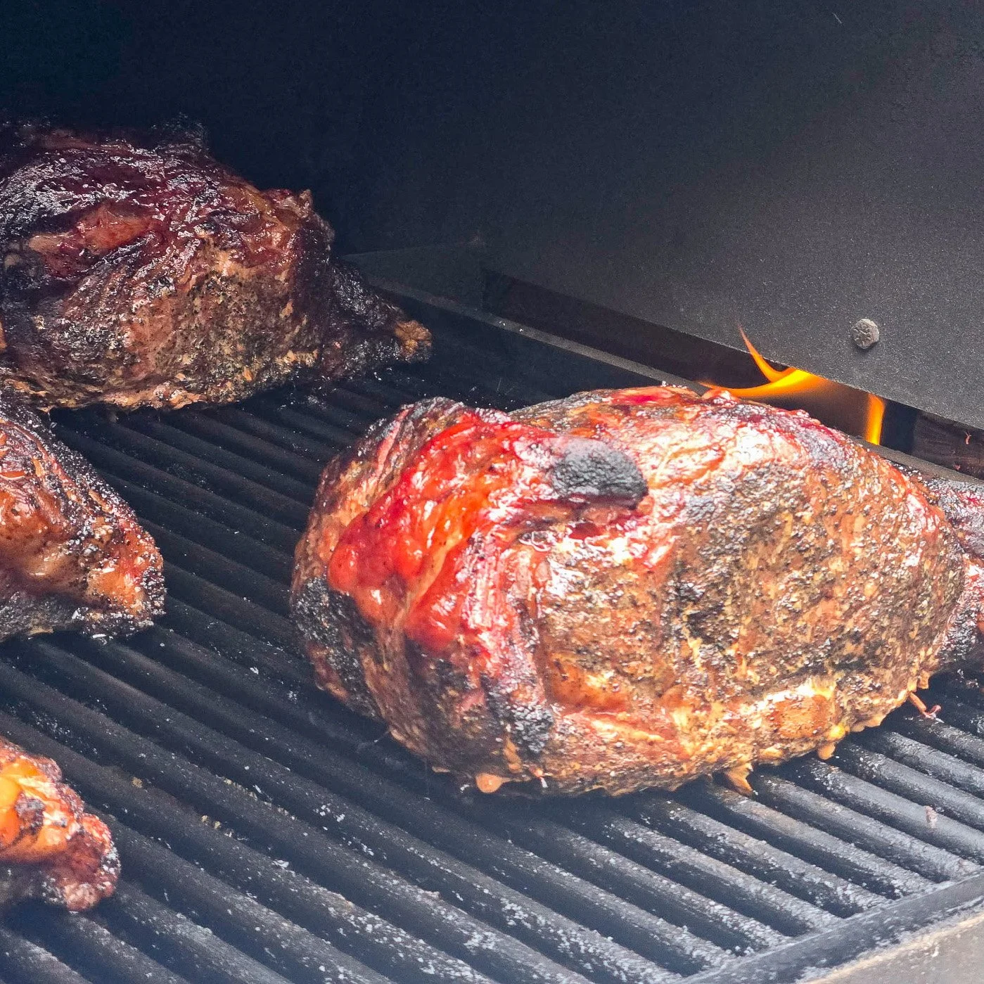 Three large cuts of meat grilling on a barbecue with grill marks and slight charring.