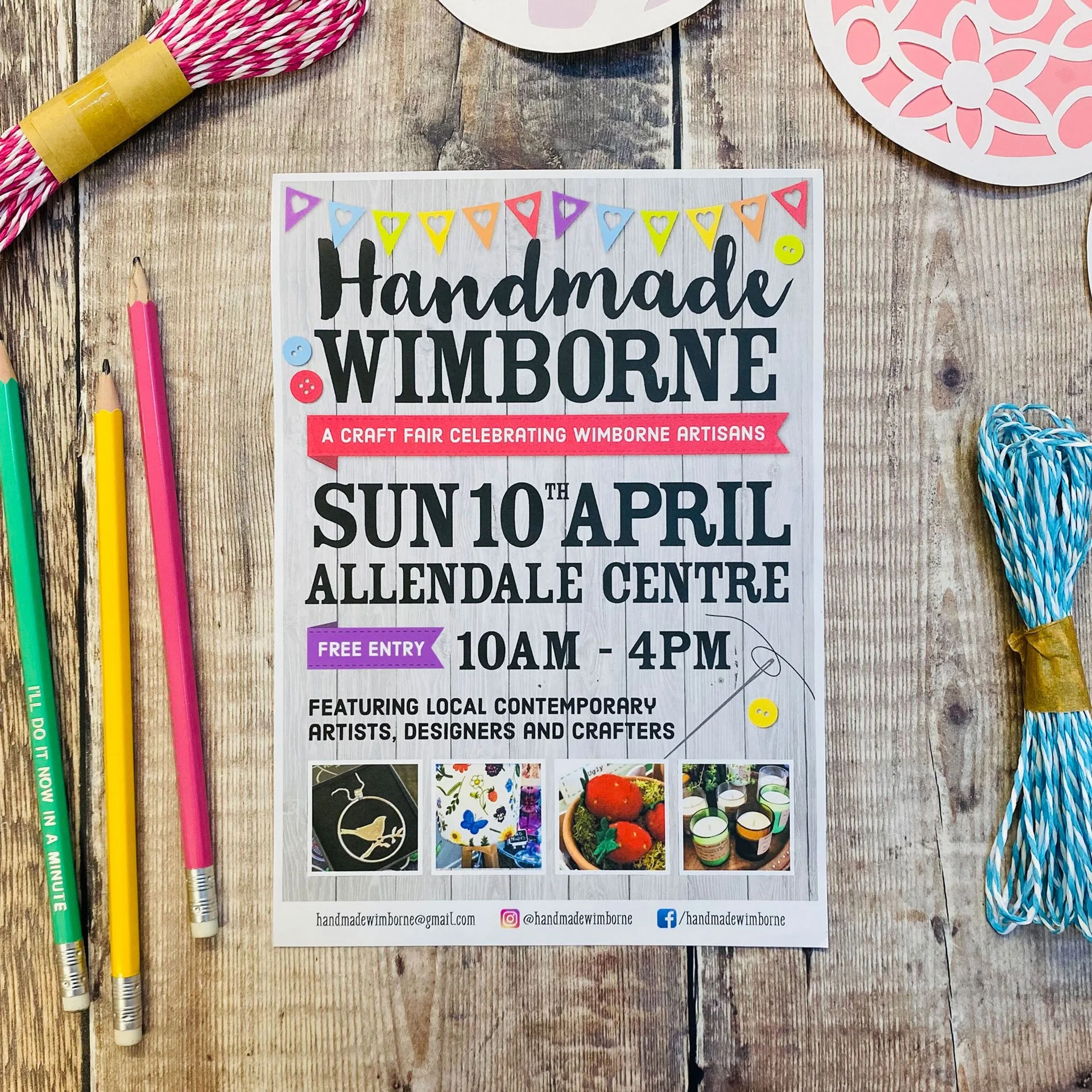 Flyer for a craft fair called "Handmade Wimborne" featuring local contemporary artists, designers, and crafters, with date and location details, contact information, and social media handles at the bottom, laid on a wooden surface with colored pencils and decorative paper around it.