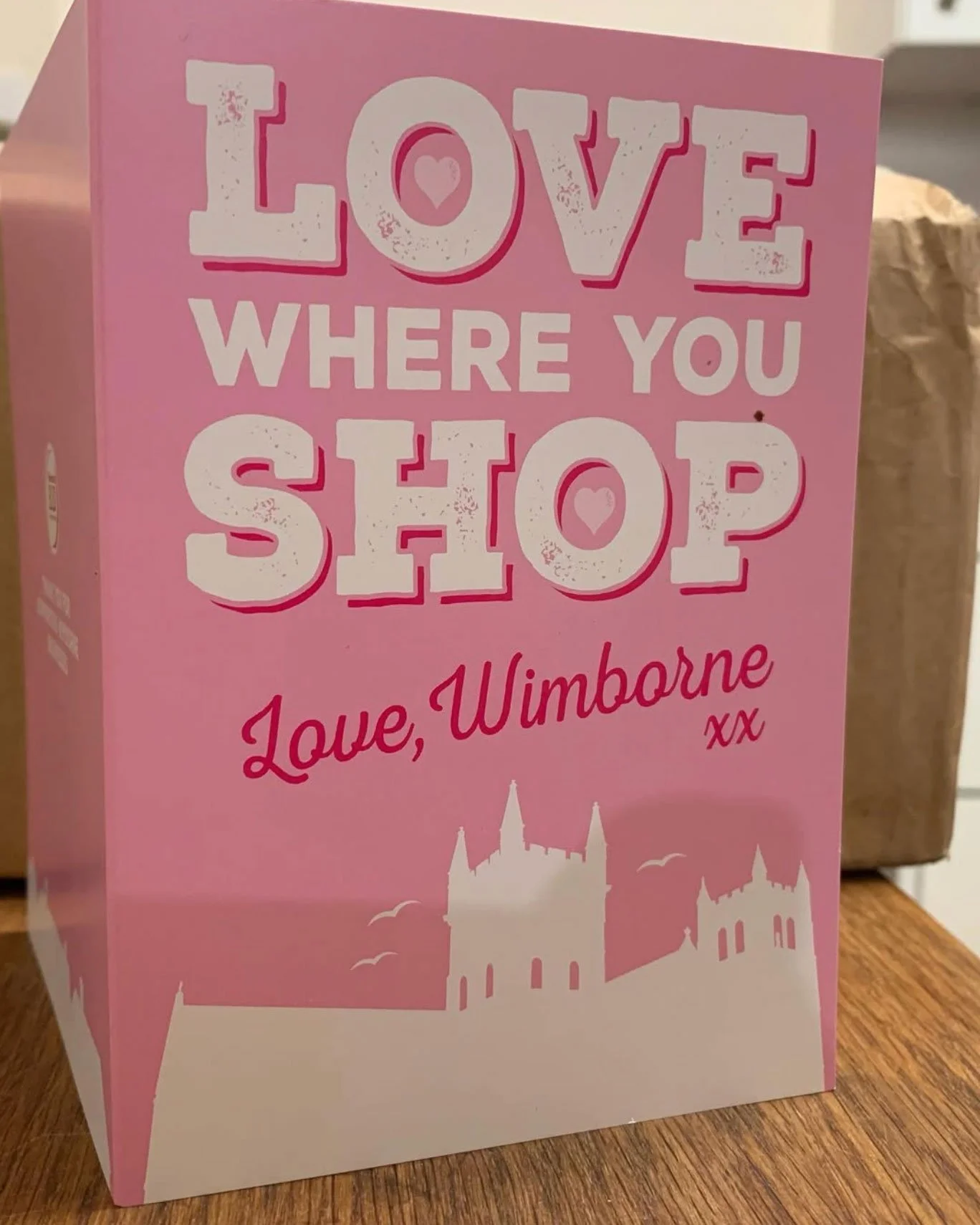 Pink box with a message about love and location, reading 'LOVE WHERE YOU STOP Love, Wimborne xx' with a silhouette of a castle and buildings at the bottom.