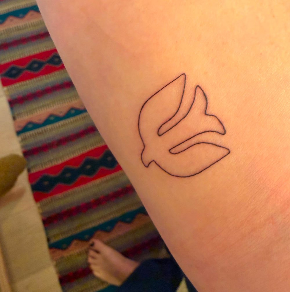 A tattoo of a swallow bird in outline on a person's forearm.