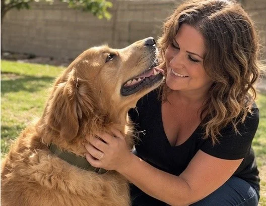 A woman smiling as she cuddles with a golden retriever dog outdoors.