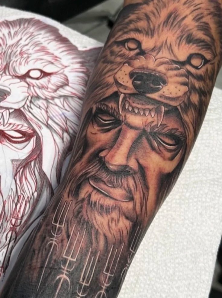 Tattoos depicting a wolf and a warrior's face on a forearm.