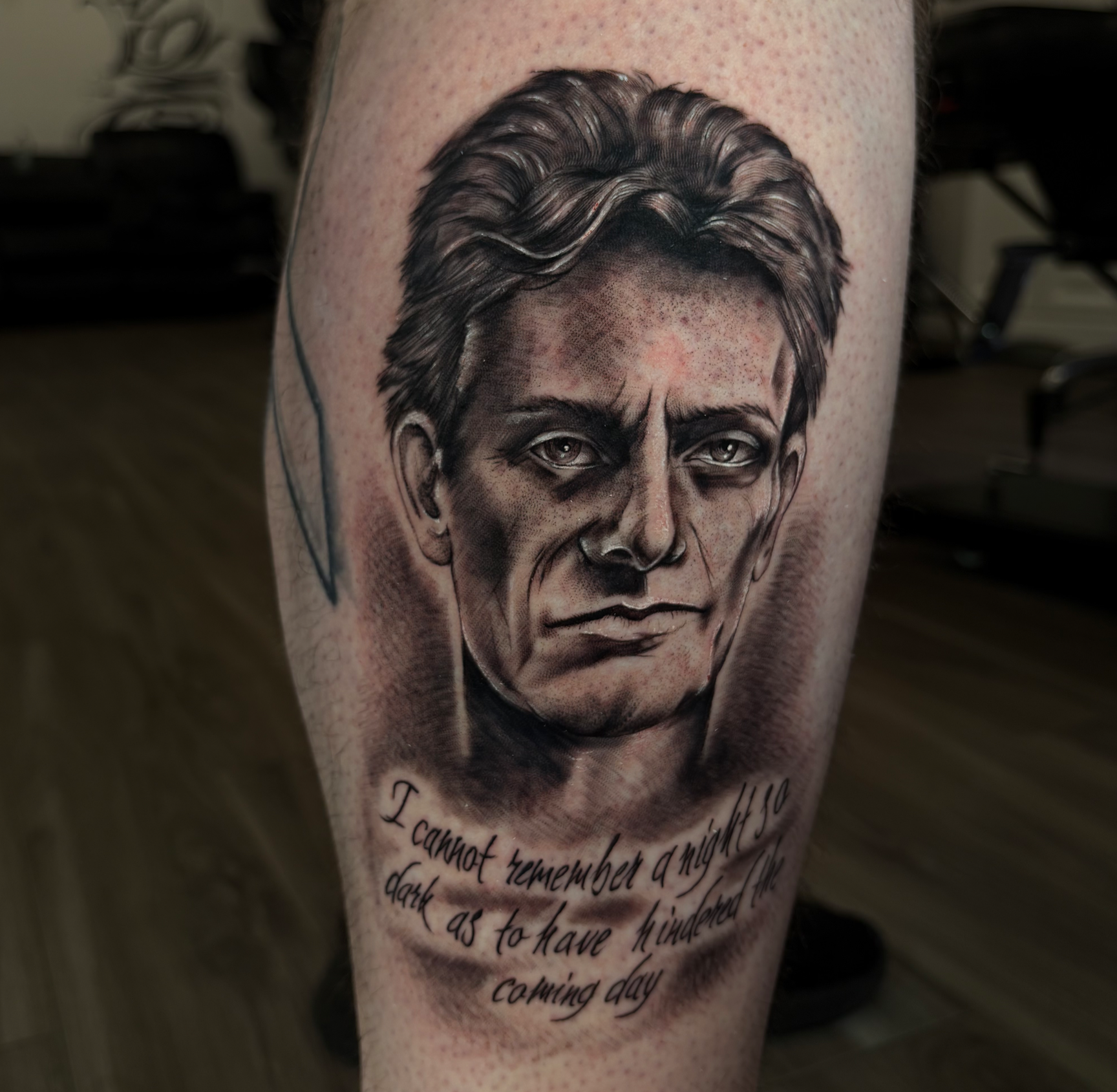 Tattoo of a man's face with text beneath it on someone's outer calf. 