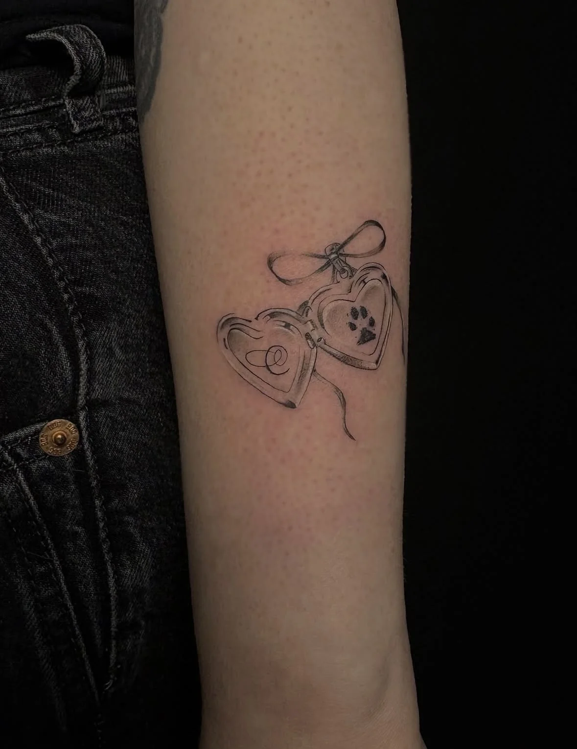 Tattoo of two hearts with a bow and a paw on a person's forearm.