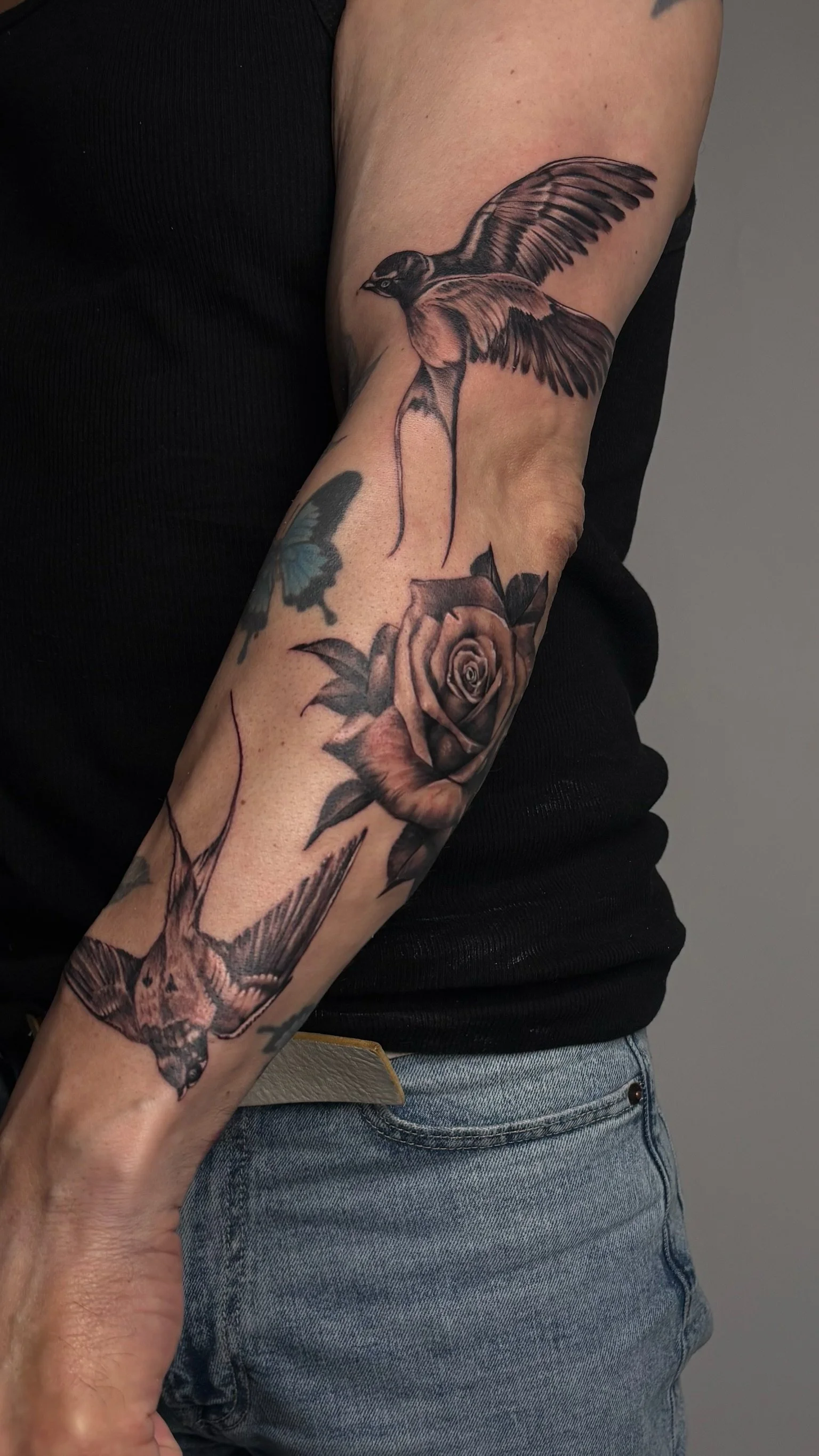 Tattoo of a realistic bird flying above a rose on forearm, creating flow and dynamic to previously started arm project.