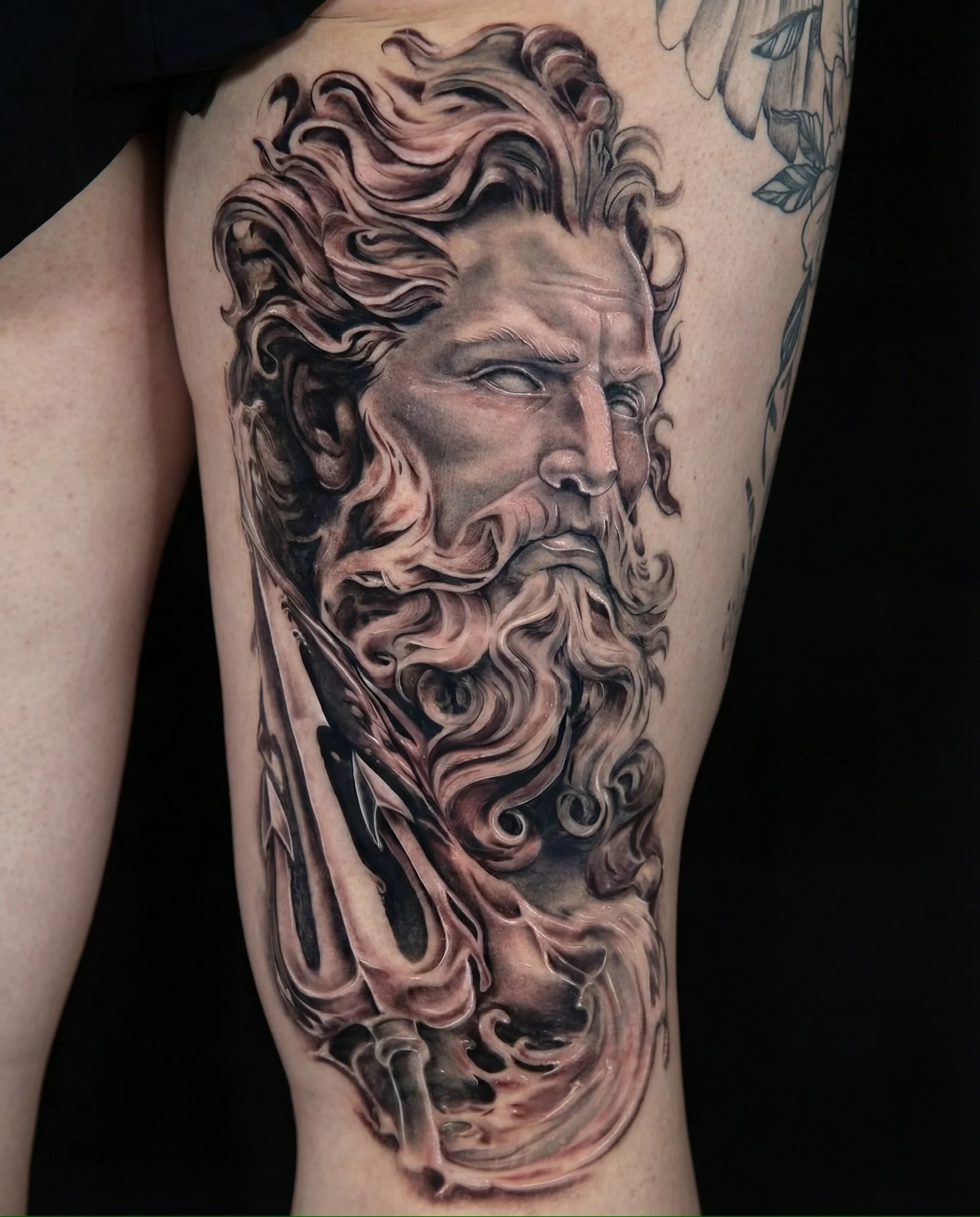 A detailed black and gray tattoo of a bearded man's face with flowing hair and a contemplative expression on the thigh.