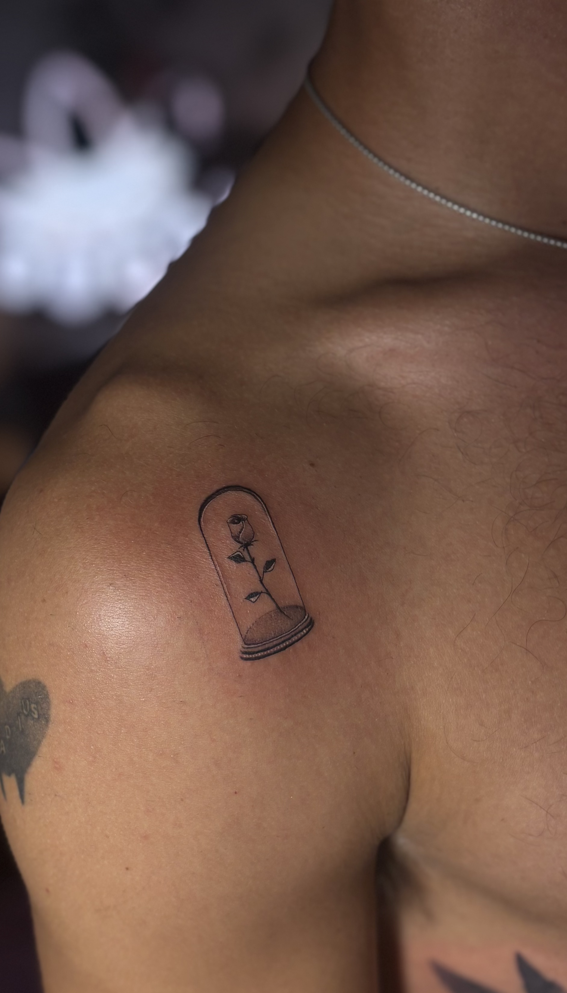 Close-up of a person's shoulder with a small tattoo of a glass terrarium containing a tiny rose inside.