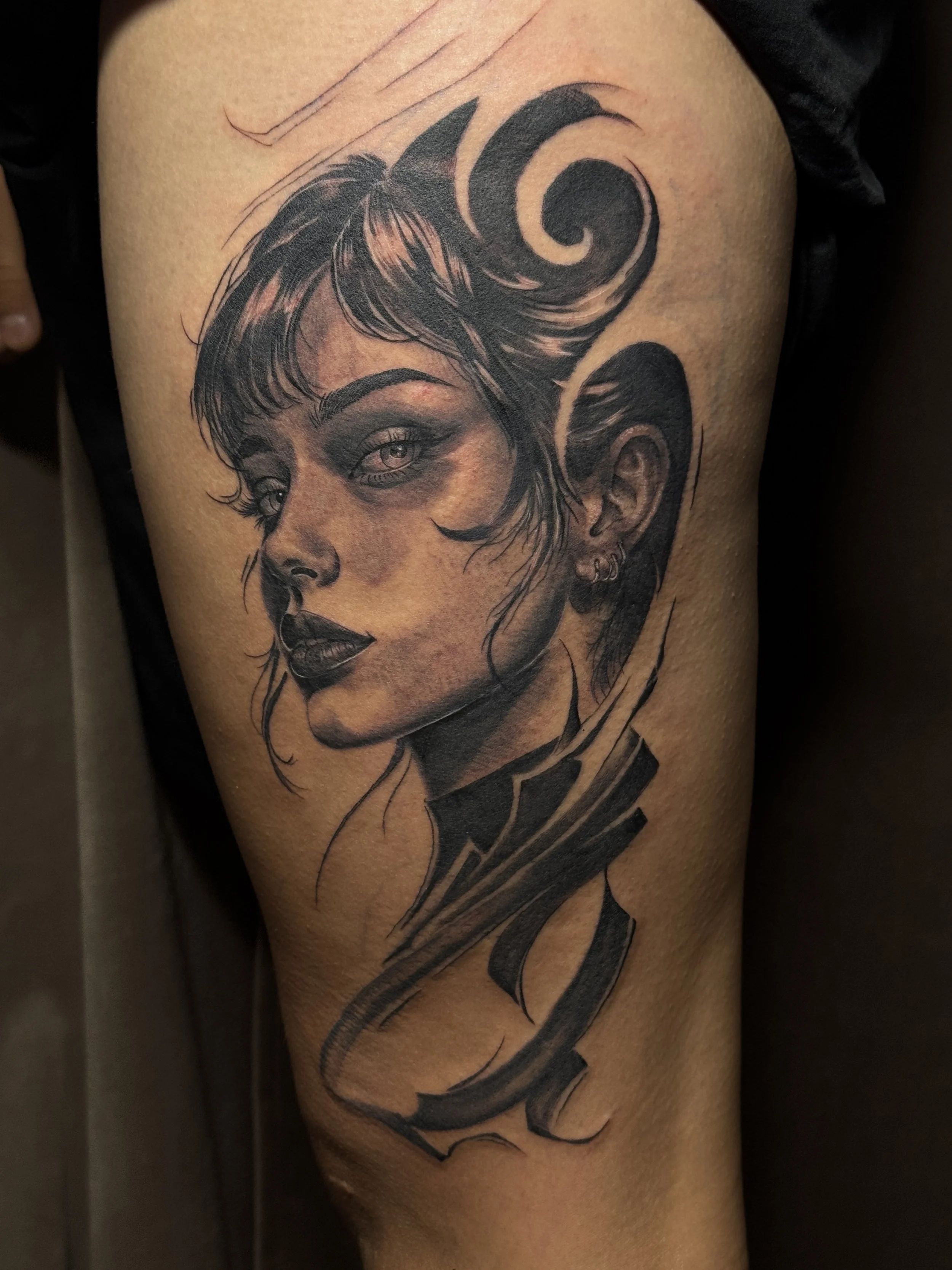 Tattoo of a woman's face with short hair, dark makeup, and earrings, surrounded by swirling design elements.