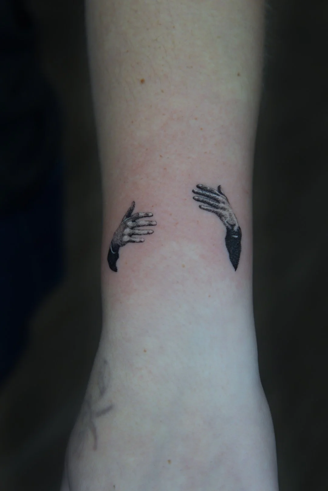Tattoo of two black and gray hands reaching toward each other, resembling a hug on a person's arm.