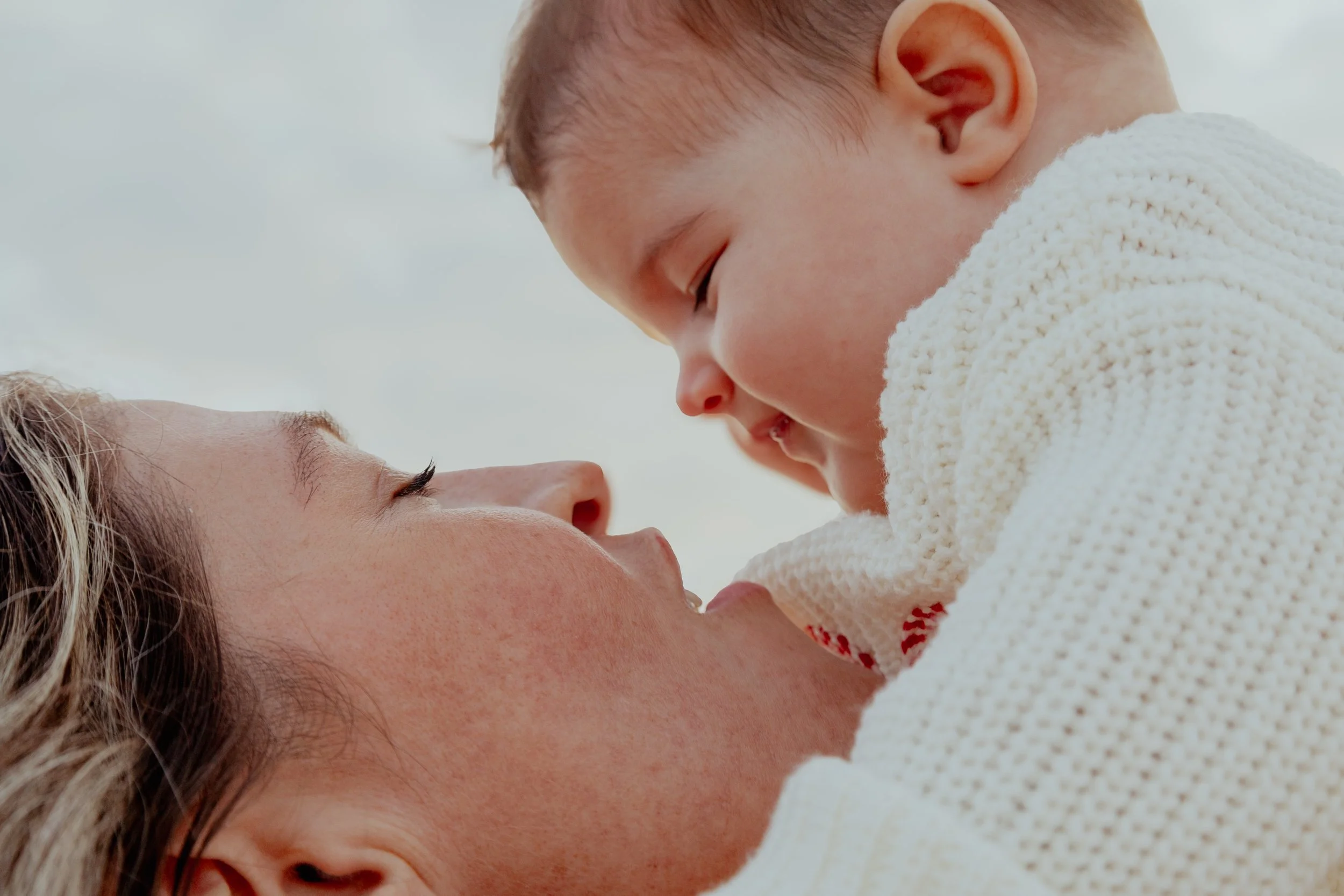 A woman lying down with a child on her shoulders, both smiling and looking at each other affectionately.