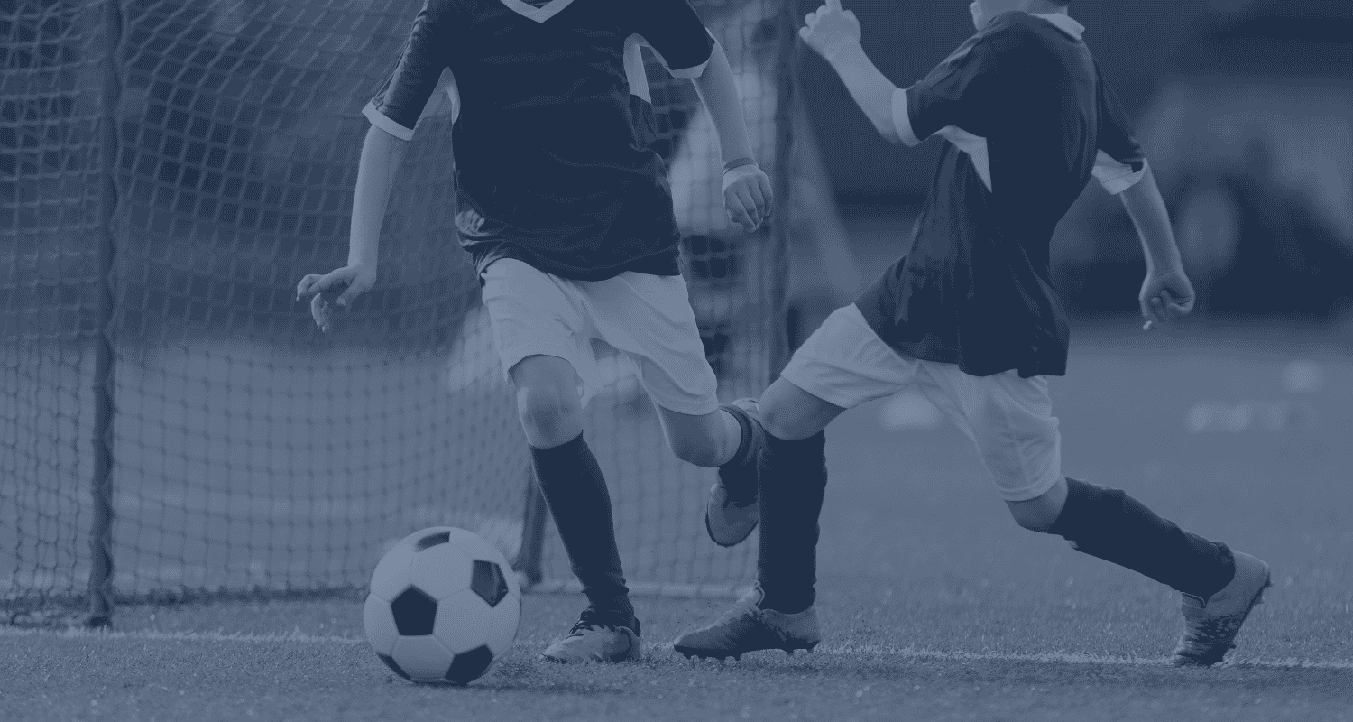 Two young soccer players competing for the ball near the goal, with a soccer net in the background.