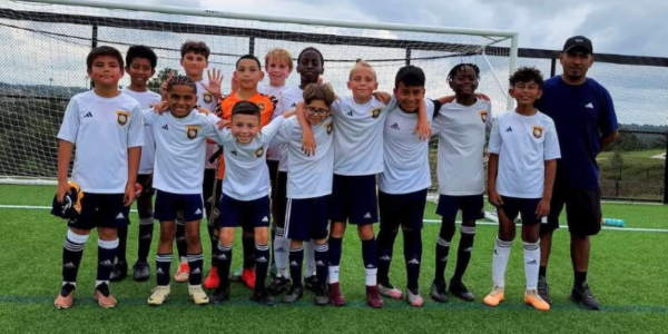 Young boys' team in soccer uniforms and a coach pose for a photo on a soccer field