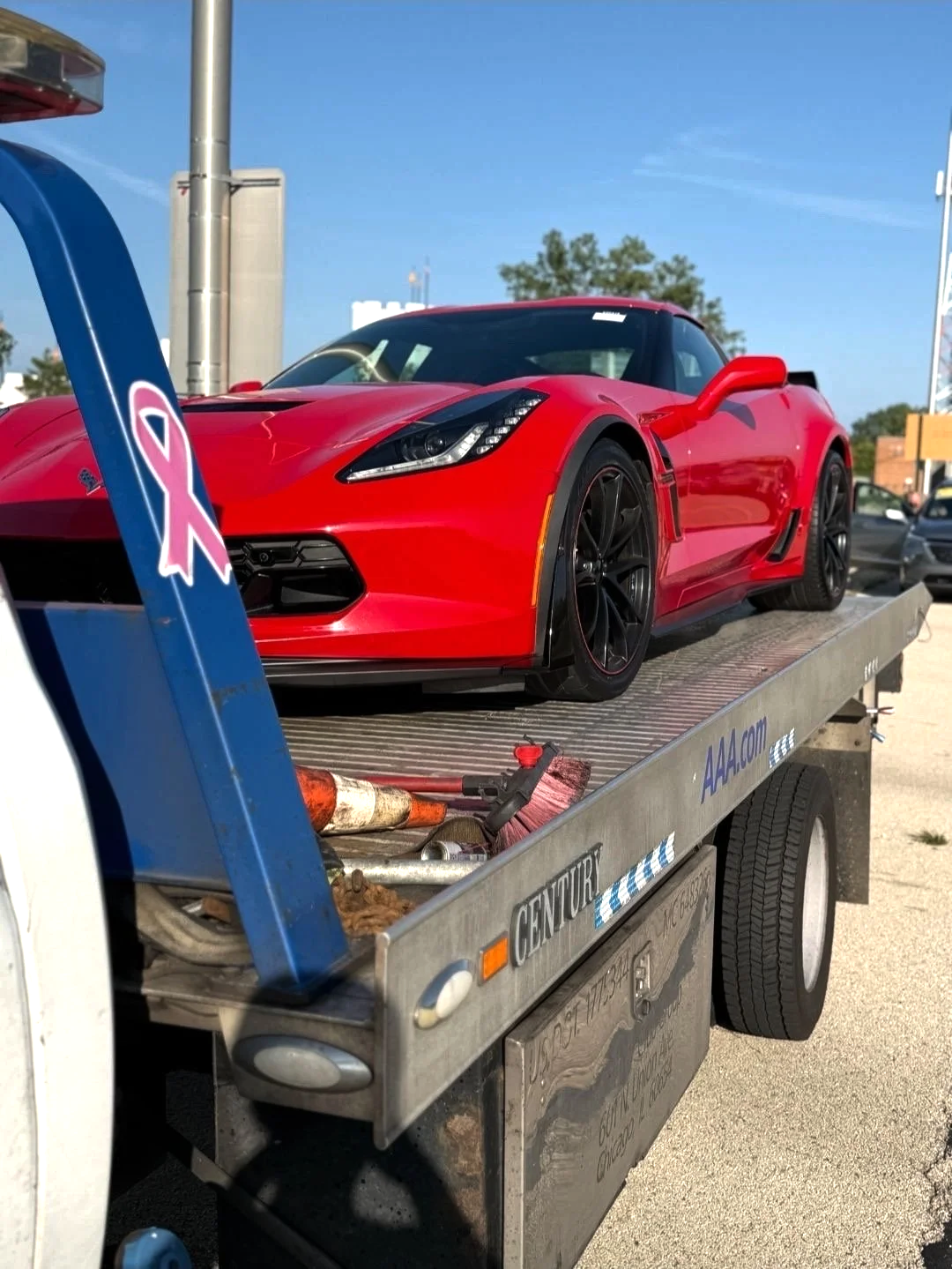 Red sports car on a flatbed tow truck in a parking lot.
