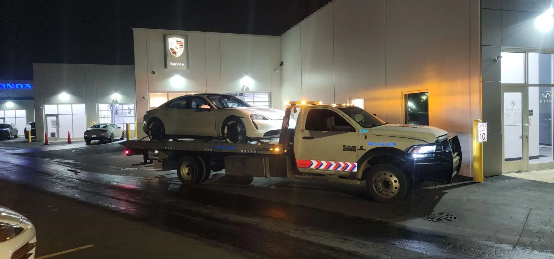 A tow truck transporting a white sports car outside a service center at night.