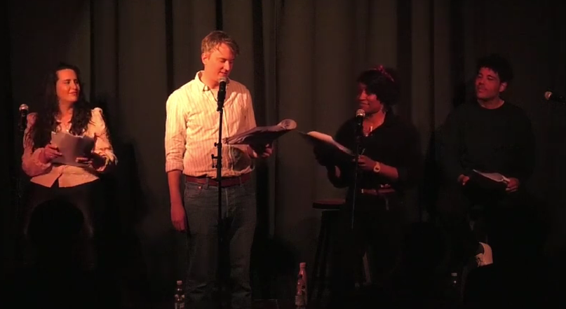 Four people on a stage with dark curtains, holding papers, and speaking into microphones during a performance event of a script a the Covent Garden Comedy Club.