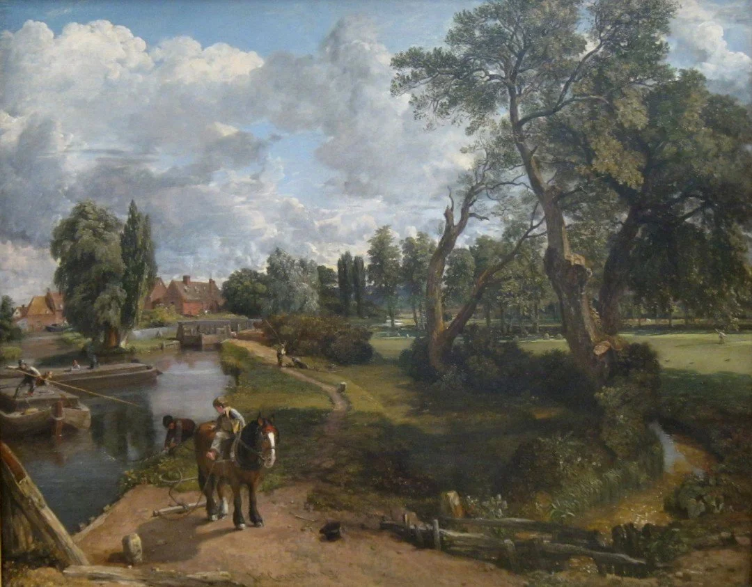 A detailed landscape painting showing a river, trees, a small stone bridge, and a few houses in the background. In the foreground, a person is washing a horse, with other figures relaxing along the riverbank. The sky is partly cloudy with sunlight illuminating the scene.
