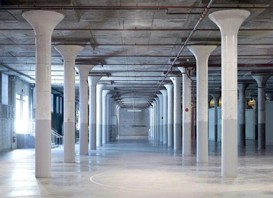 Empty indoor arts space with tall white columns and wooden ceiling. Part of Dia Arts Foundation.