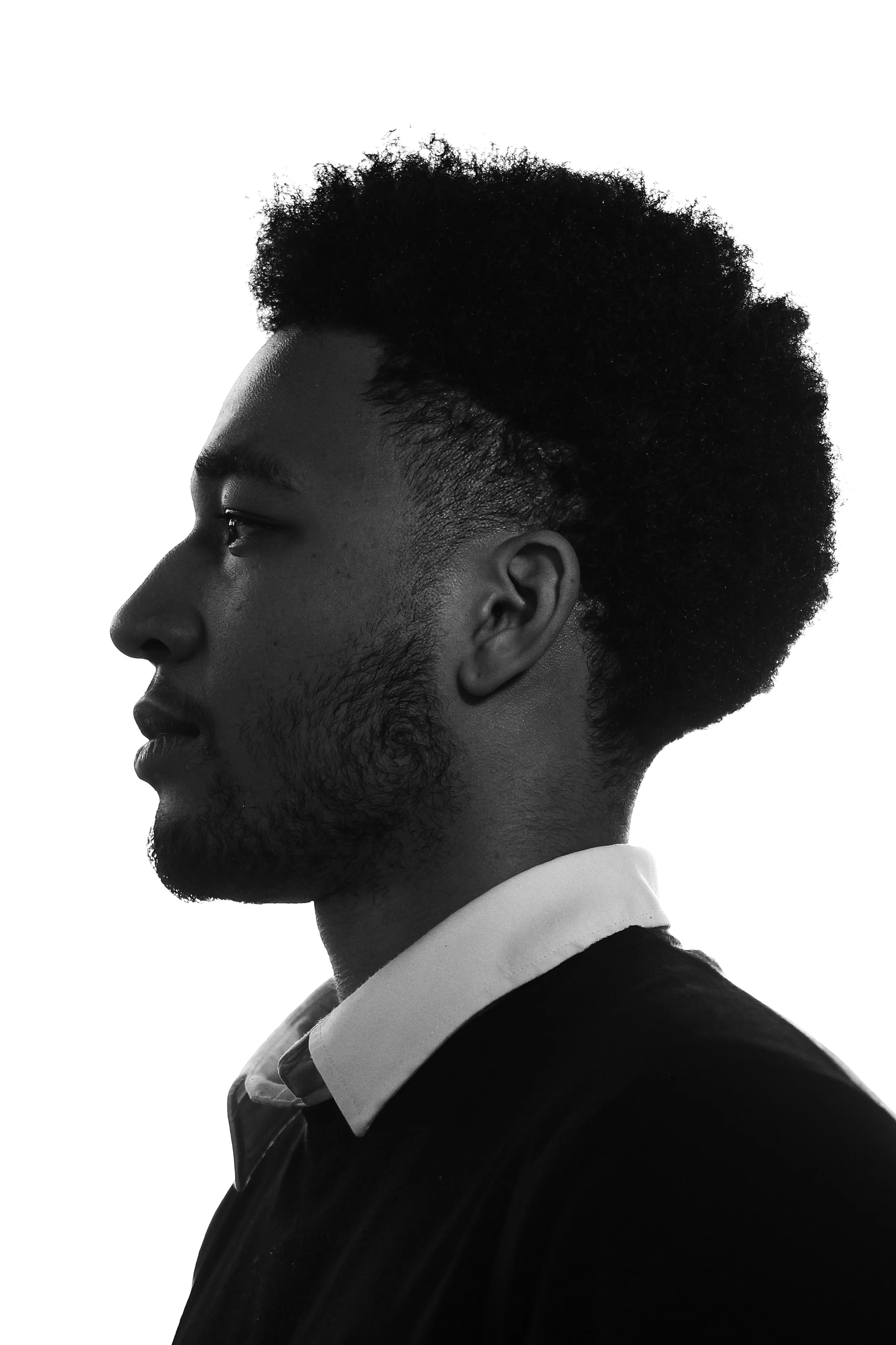 Black and white side profile of a young man with curly hair, wearing a dress shirt and jacket.