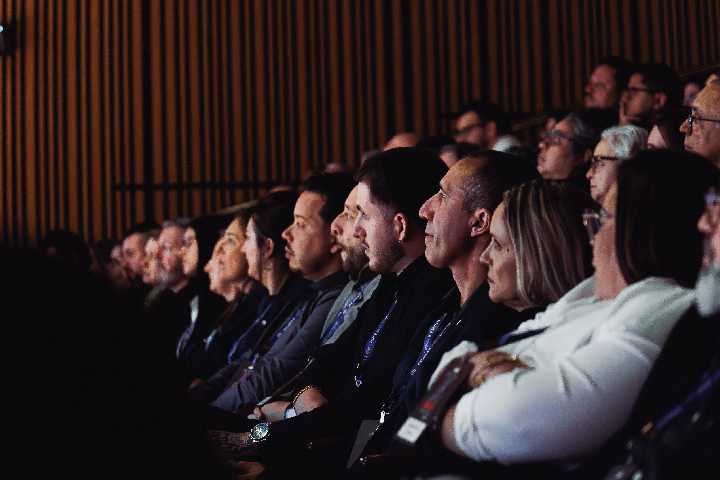 Audience seated in a dark auditorium, attentively watching a presentation or performance.
