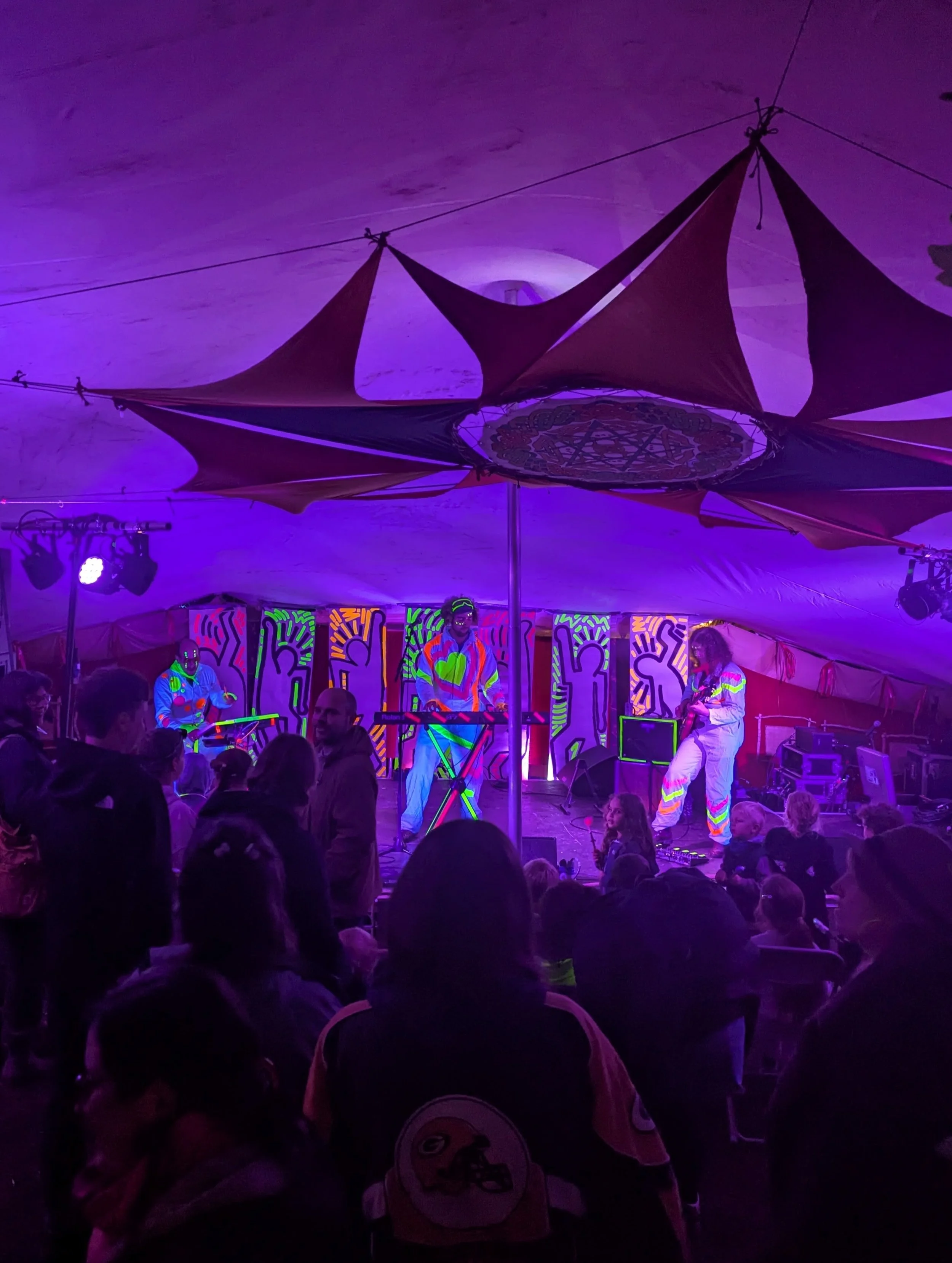 A live music performance in a colorful, vibrant setting with neon and fluorescent lighting, where musicians are playing instruments.