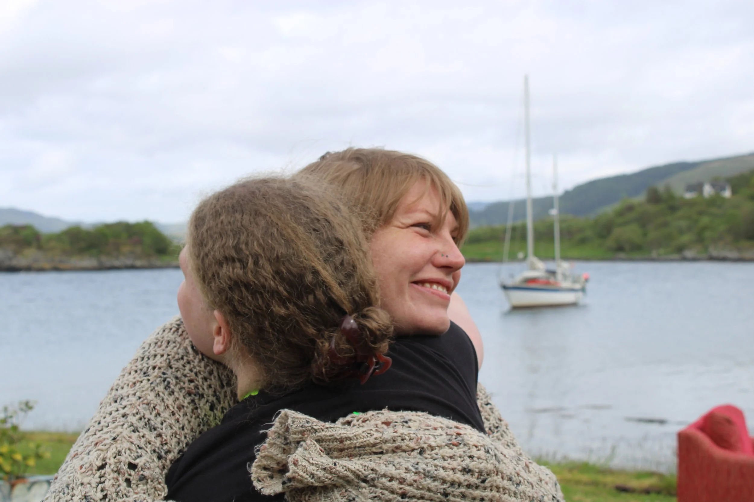 Two people hugging with a lake and sailboat in the background.