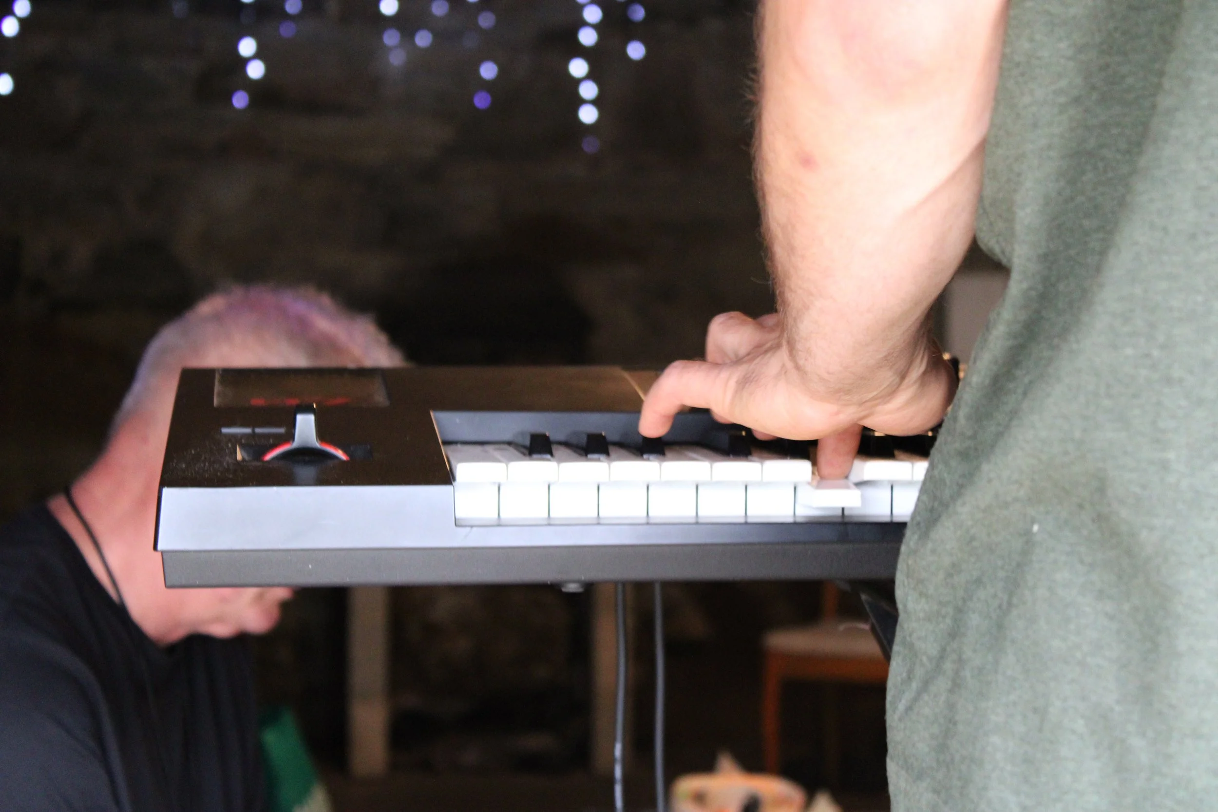 A person playing an electronic keyboard, with the tech team partially visible beside them.