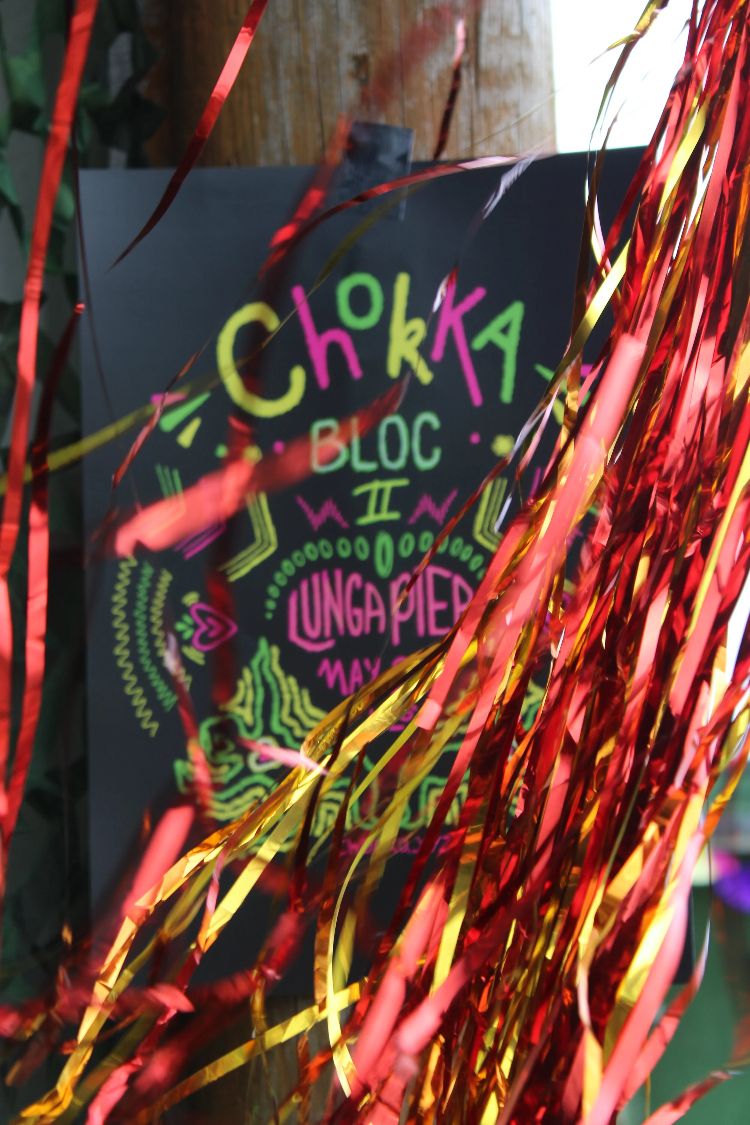 Colorful, neon sticker or poster partially hidden behind red and yellow foil streamers. The words "CHAKKA BLOC II" are visible.