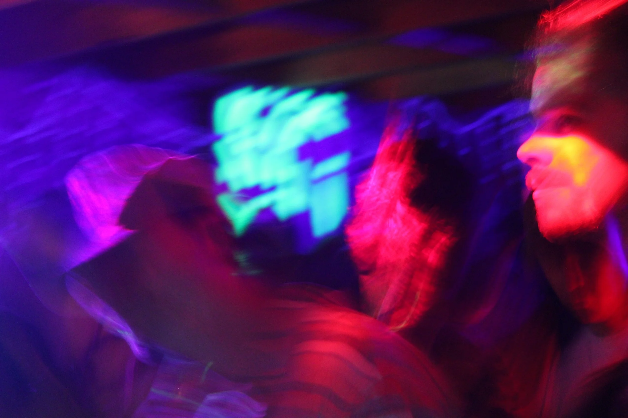 A person wearing glasses with neon lights reflecting on their face, creating colorful light streaks in a dark background.