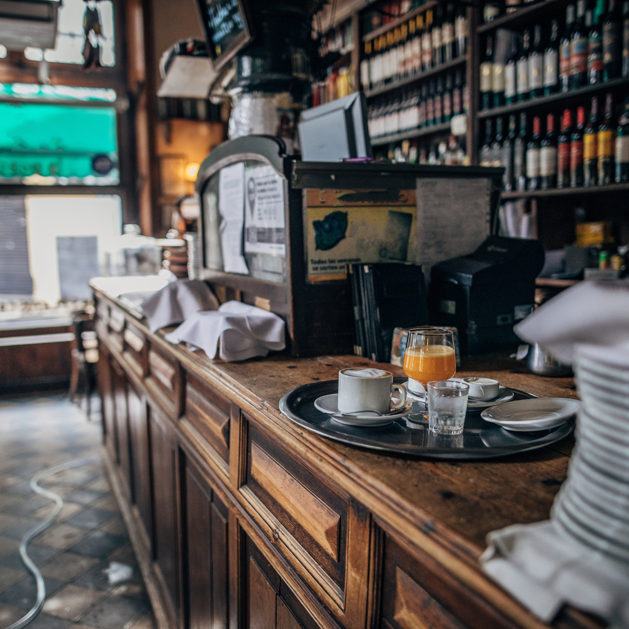 Interior of a coffee shop with a wooden counter, shelves filled with bottles, and a drink with orange juice on the counter.