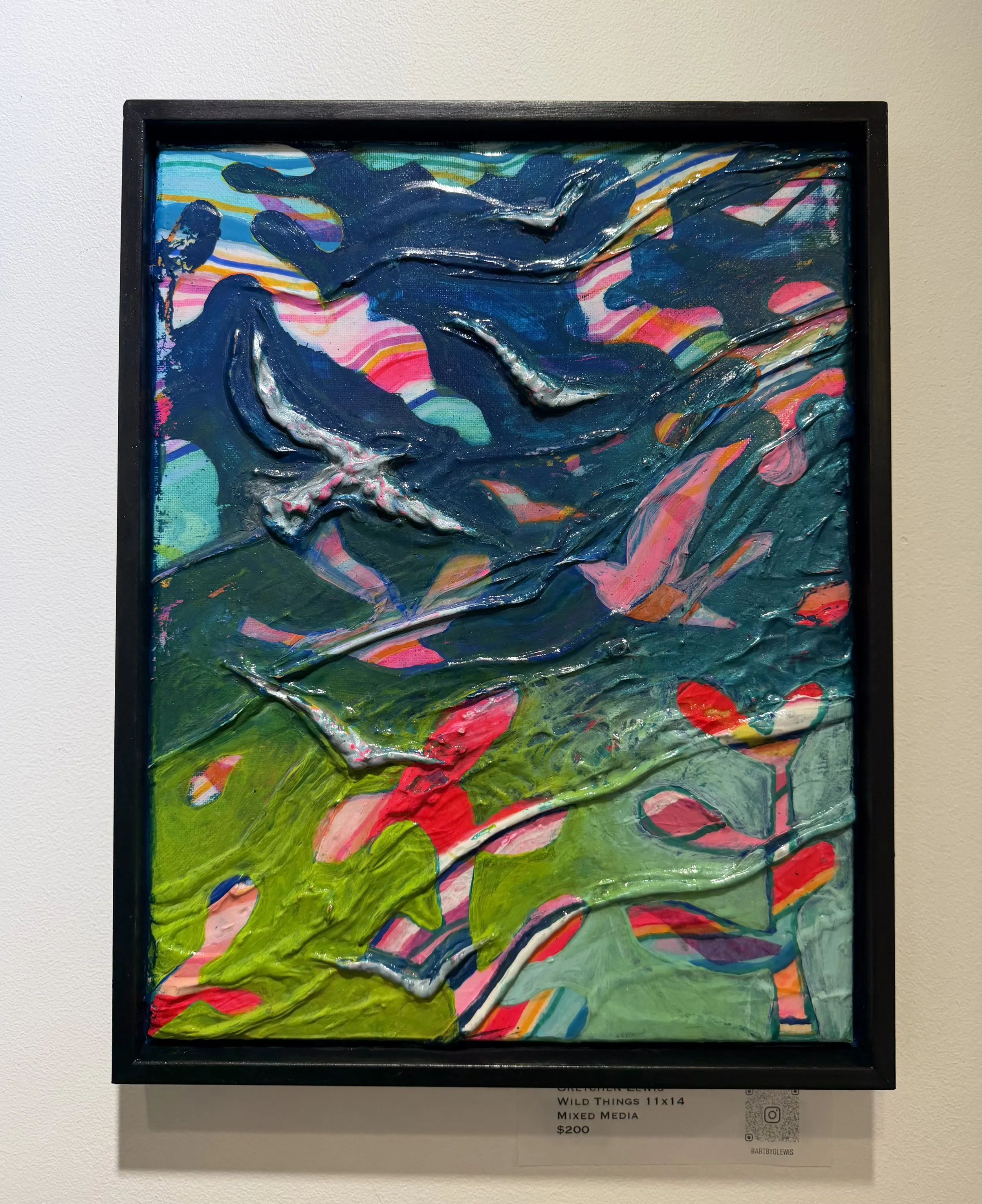 Colorful abstract mixed media artwork featuring a dark blue hand and arm against a vibrant background with swirling patterns, pinks, greens, blues, and oranges, framed in black.