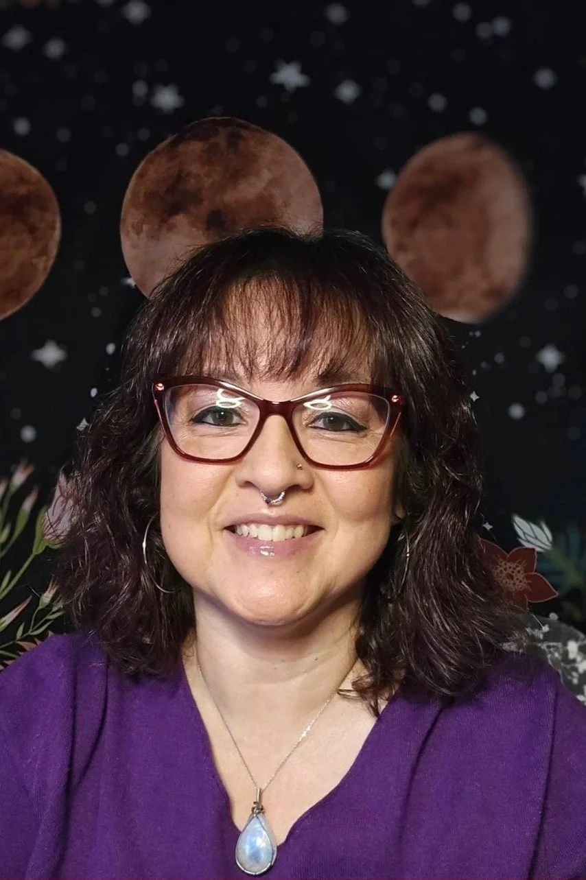 Woman with brown hair, wearing glasses, a septum piercing, and a purple top, smiling, against a space-themed background featuring planets and stars.