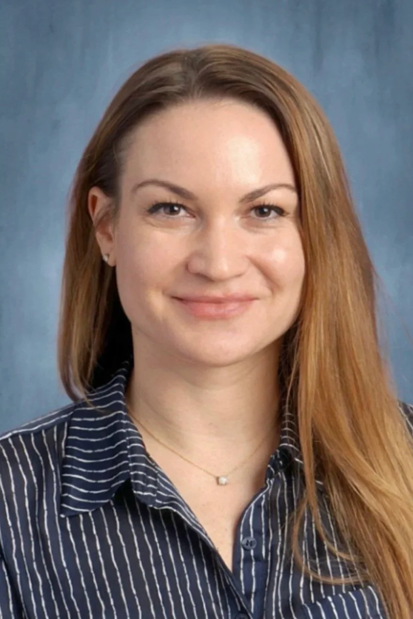 A woman with long red hair, wearing a black and white striped shirt, smiling, with a blue background.